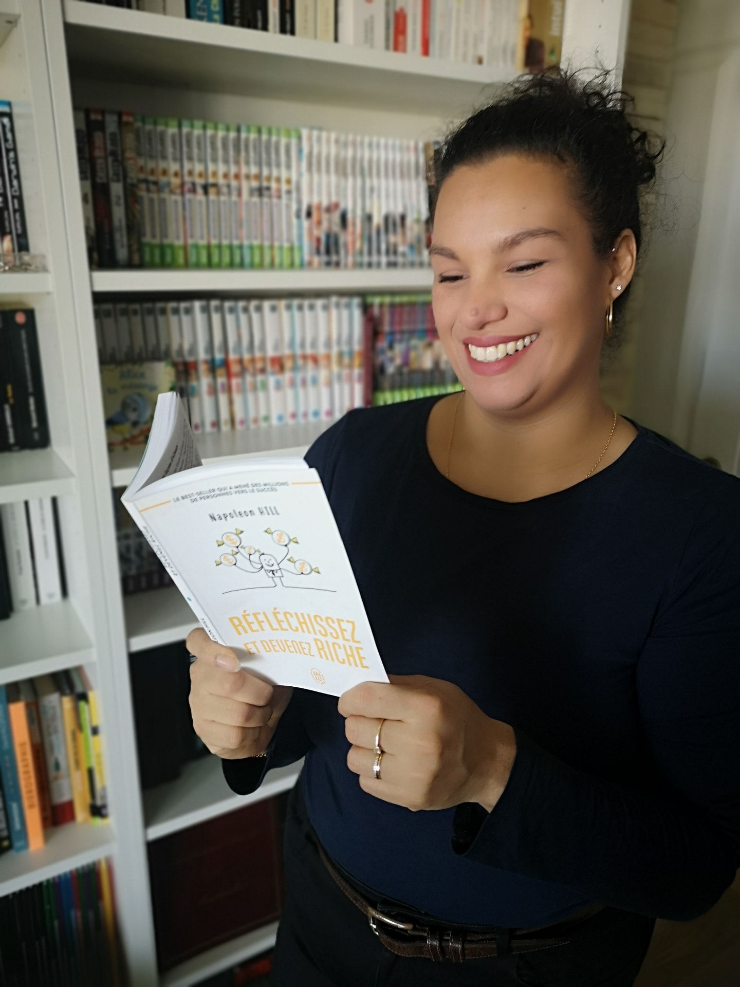 Elsa, souriante devant sa bibliothèque, un livre à la main